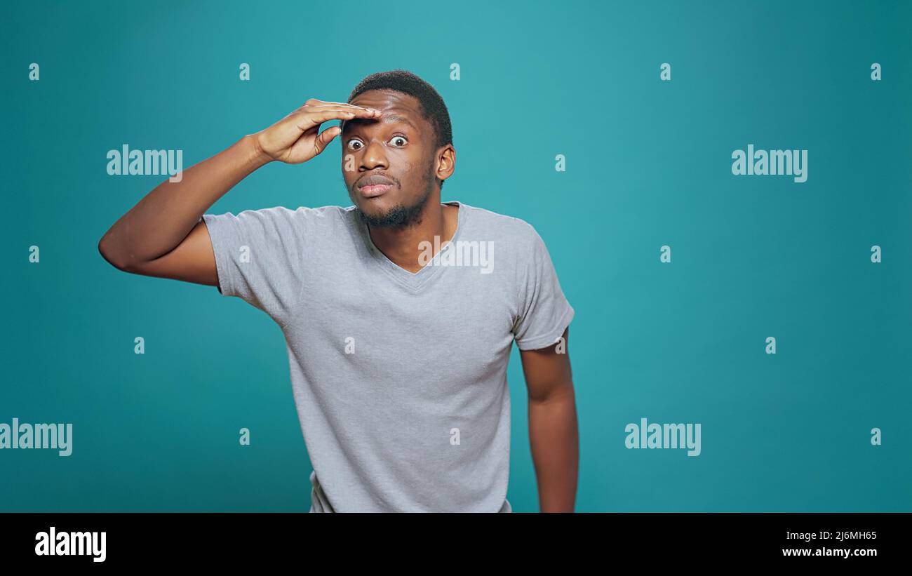 Confused person using hand over forehead to look around, searching for clue  in distance. Young adult looking forward, having interest in exploration  and feeling pensive, confident man with curiosity Stock Photo -