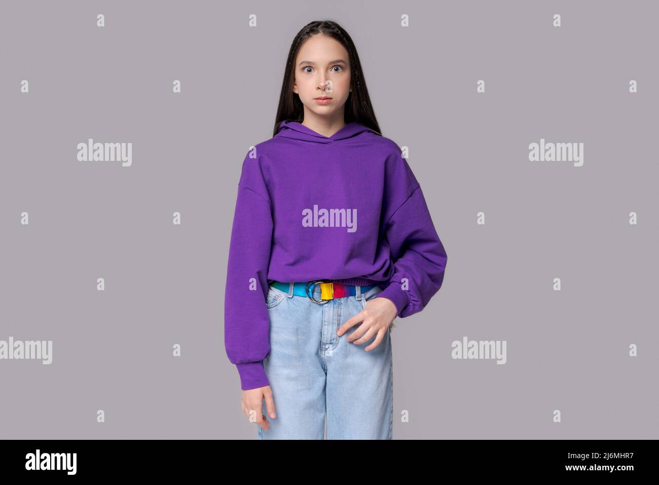 Portrait surprised young European woman looking at camera on gray space, gesturing with her hand, with a pleasant look, wearing sweatshirts, posing in the studio, having an intriguing plan in mind. Stock Photo