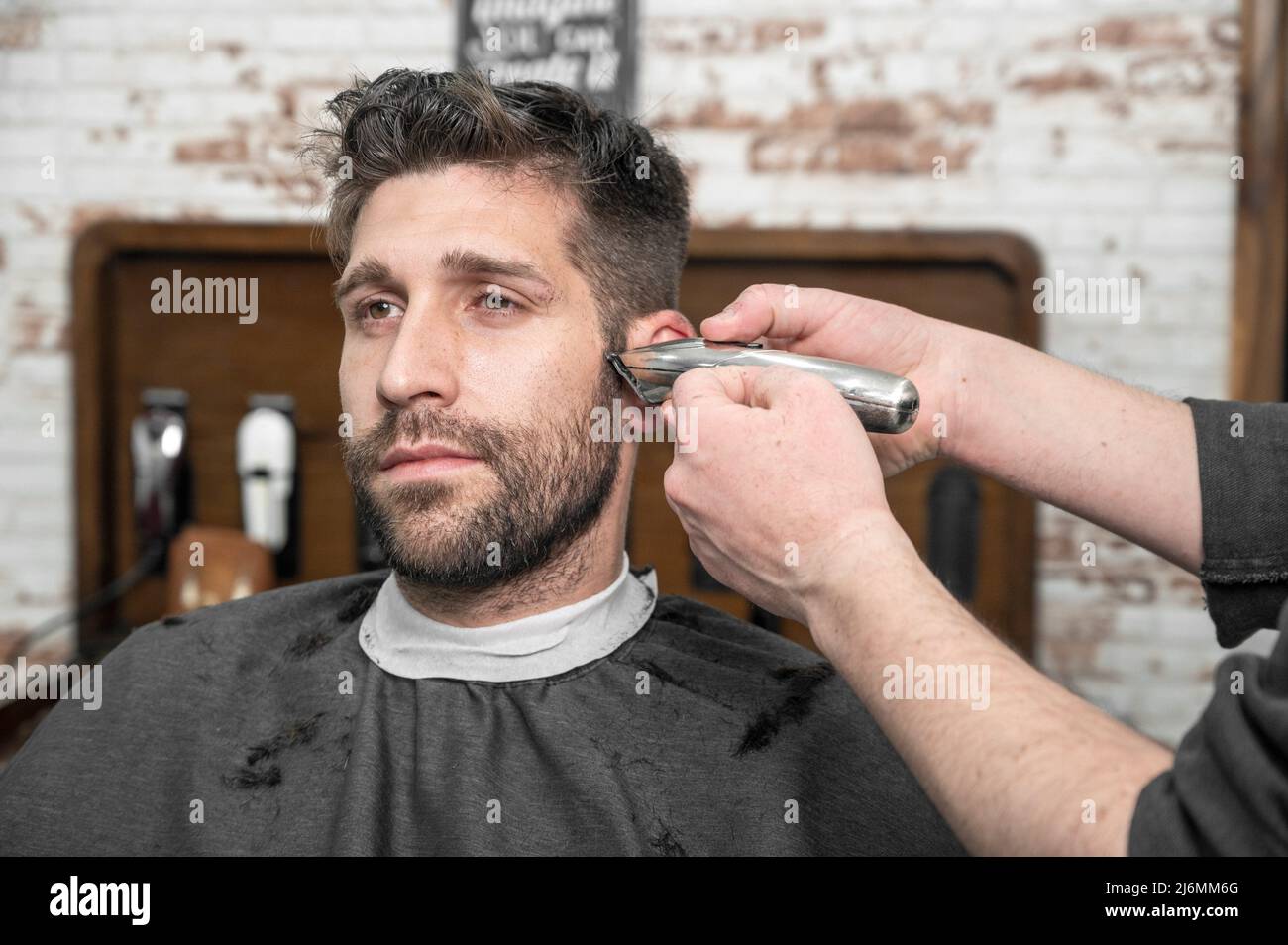 Man barber cutting hair of male client with clipper at barber shop. Hairstyling process. High quality photography. Stock Photo