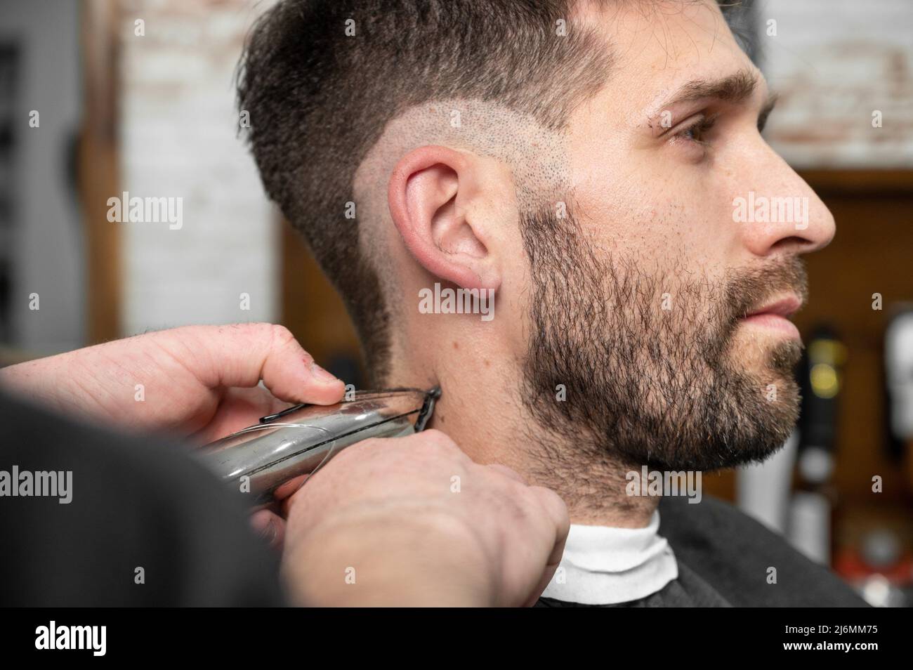 Man barber cutting hair of male client with clipper at barber shop. Hairstyling process. High quality photography. Stock Photo