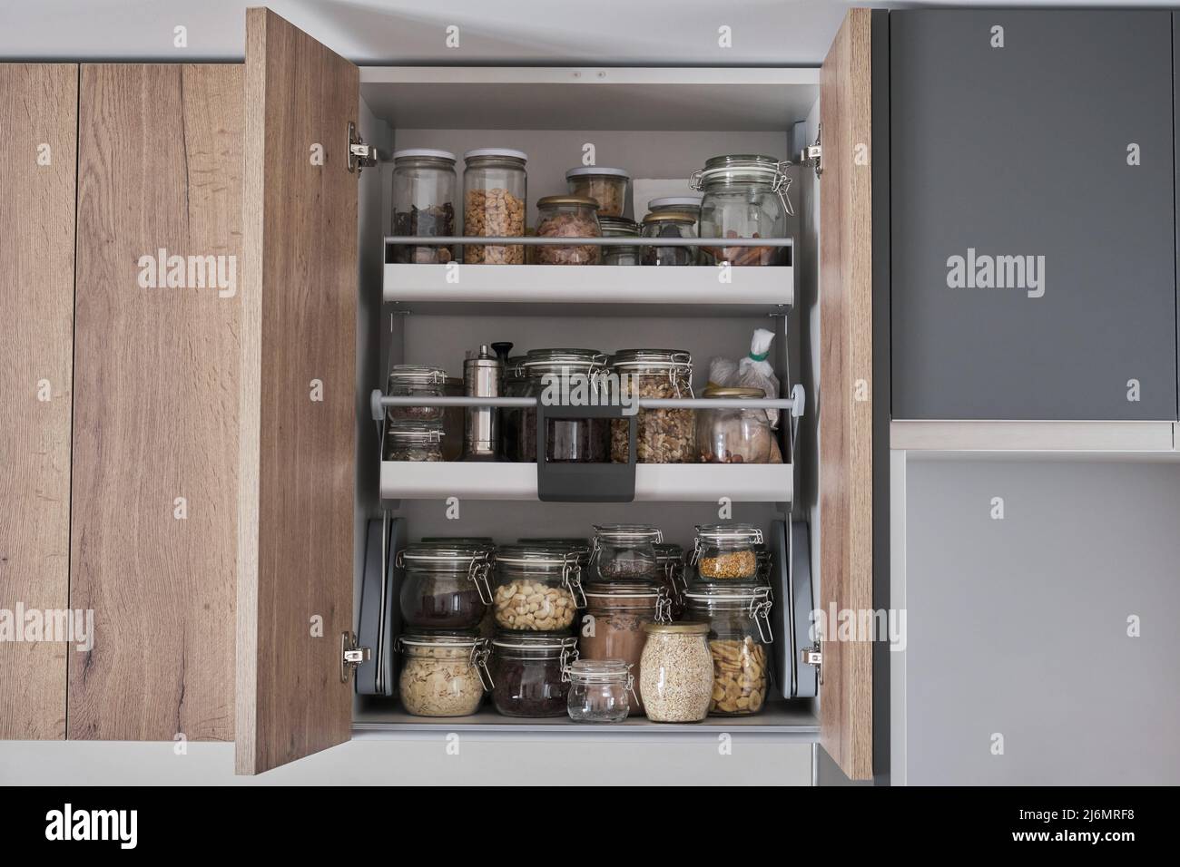 Variety of dry foods, grains, nuts, cereals in glass jars in kitchen cupboard. Stock Photo
