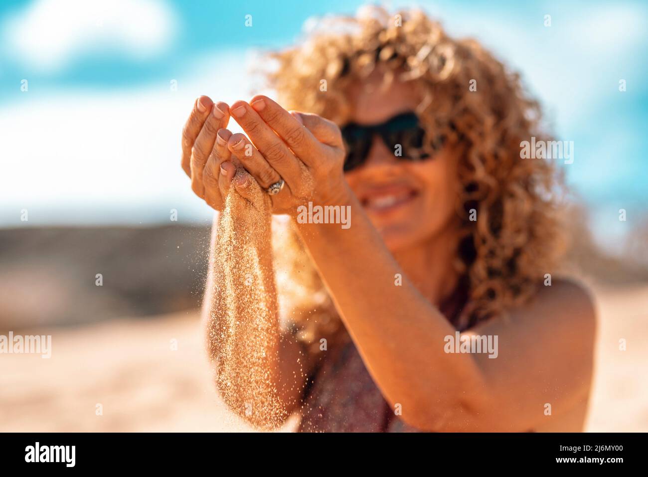 Summer holiday vacation travel woman lifestyle in outdoor leisure activity playing with the sand at the beach. Focus on hands and sand going down. Stock Photo