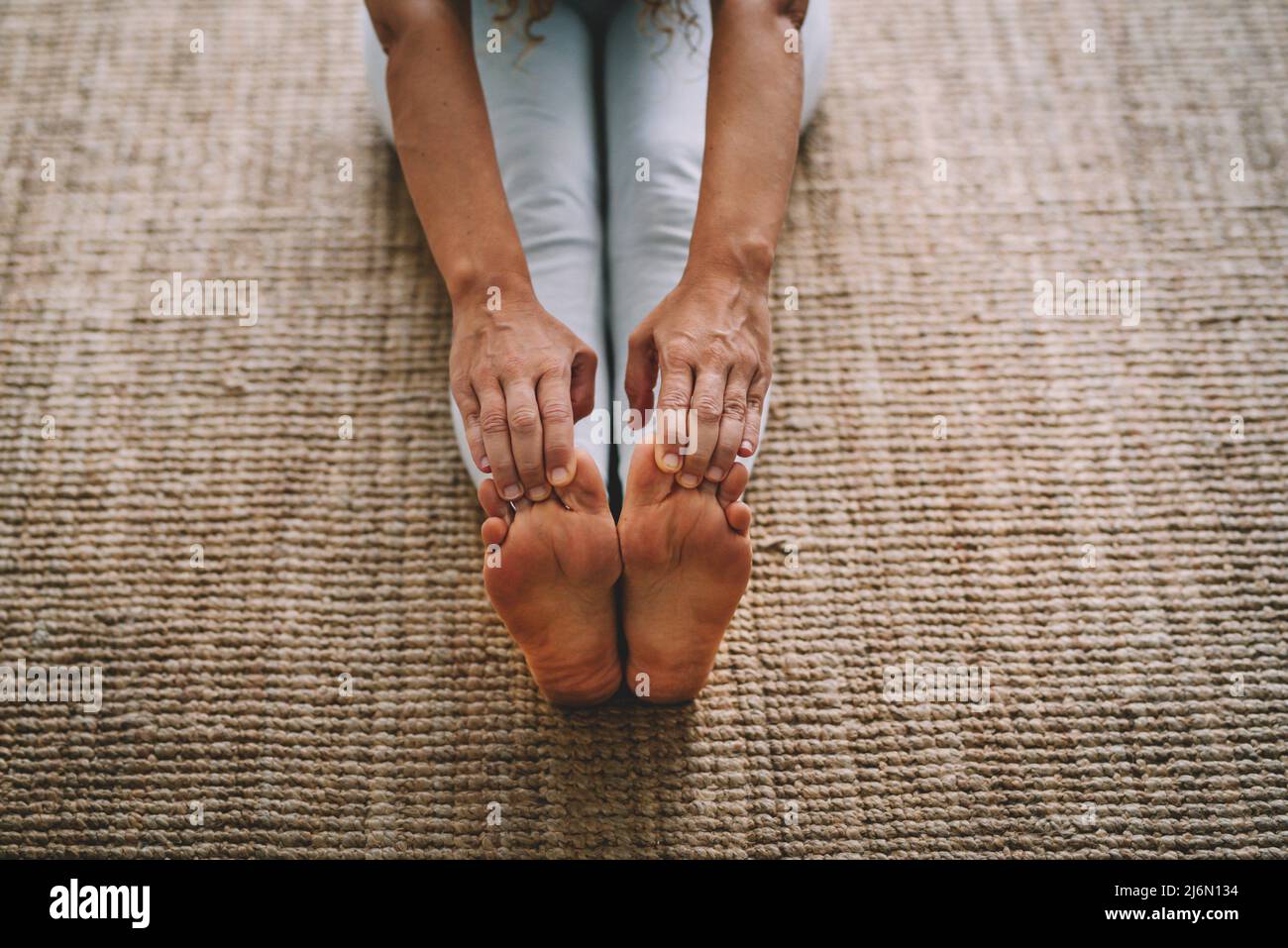 Adult mature woman and fitness healthy activity at home. Female on teh carpet touching her feet with hands for active workout active lifestyle. Stock Photo