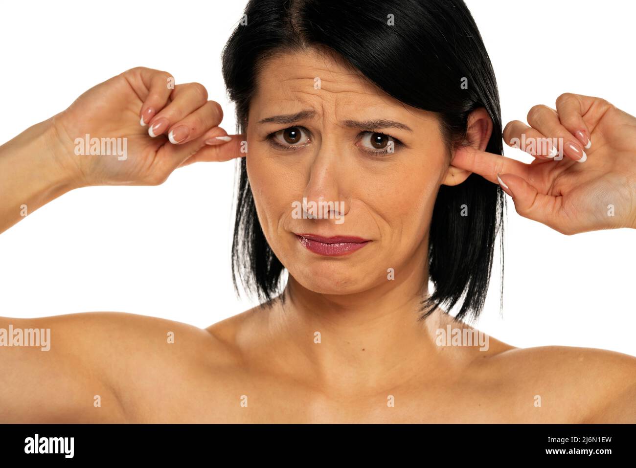 Portrait of disturbed young woman putting fingers on the ears on white background. Stock Photo