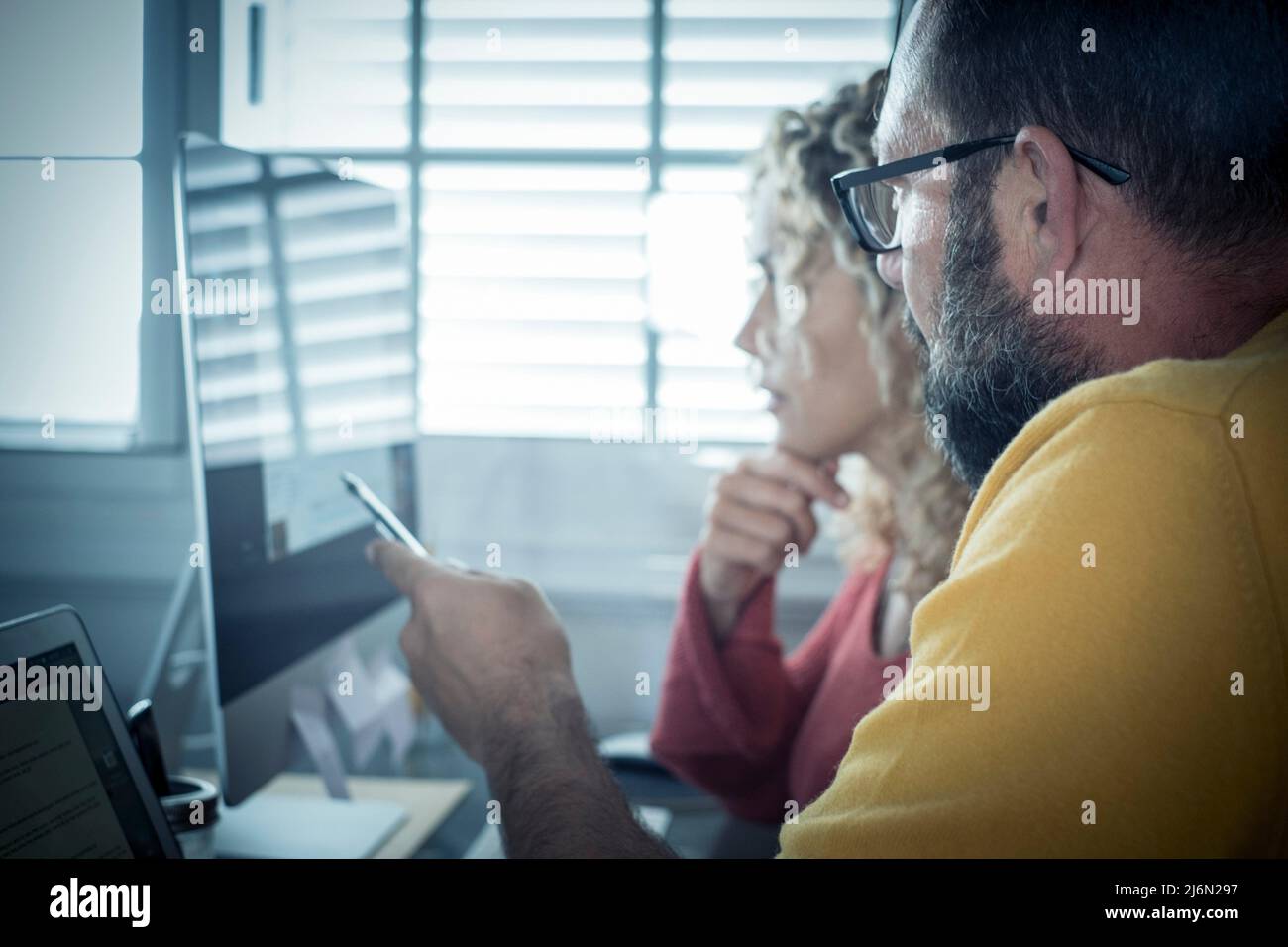 Smart working at home free office lifestyle with adult couple using home and two pc laptop computer on the desktop - modern man and woman online job Stock Photo