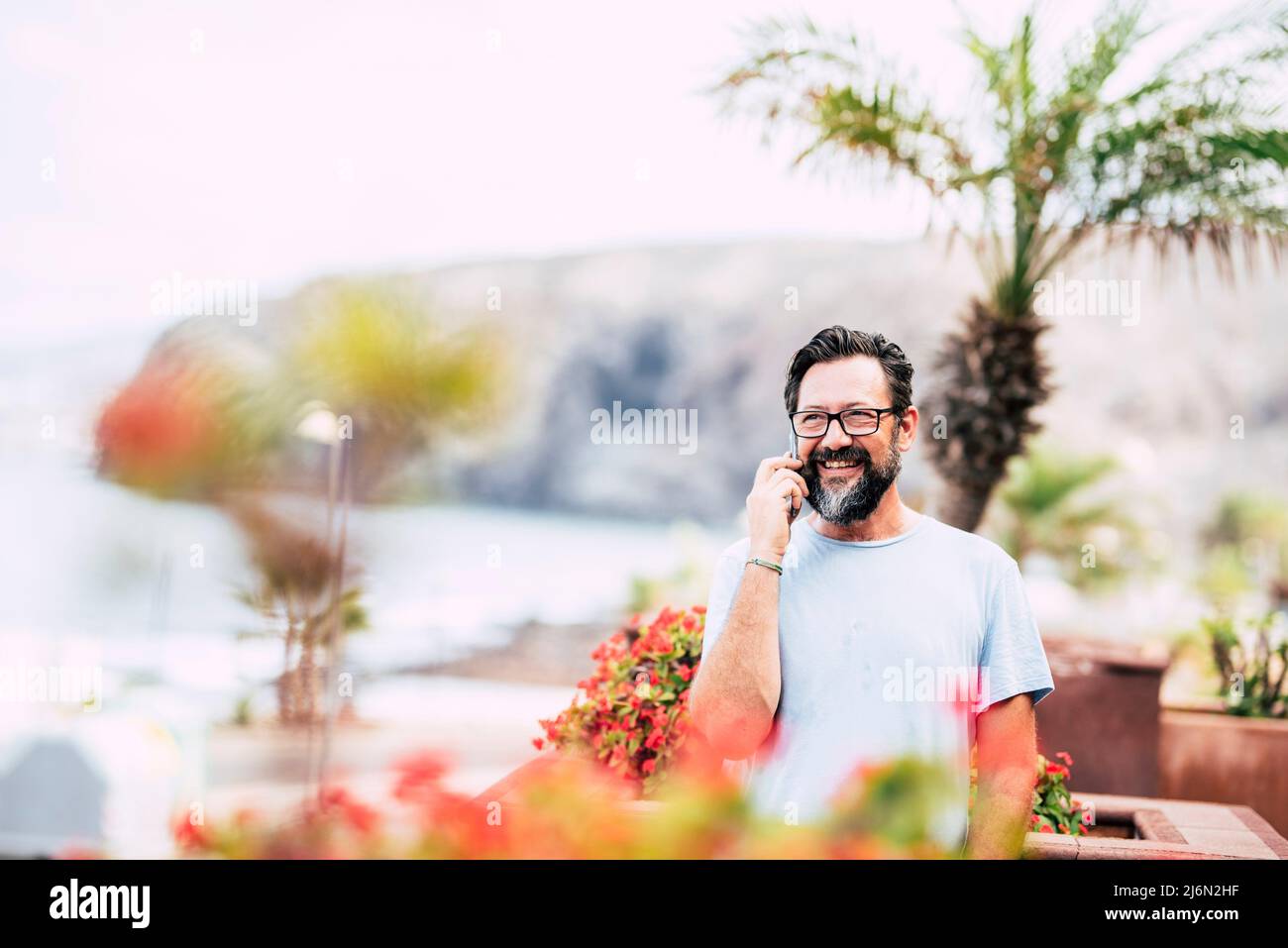 Cheerful handsome portrait of caucasian people man do phone call outdoor in the garden - young male with glasses use cellular and smile. Stock Photo