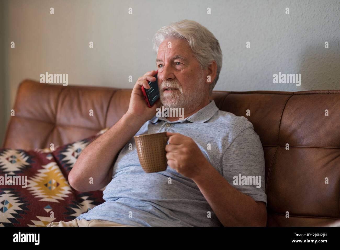 Serious senior aged man doing phone call sitting at home with smart