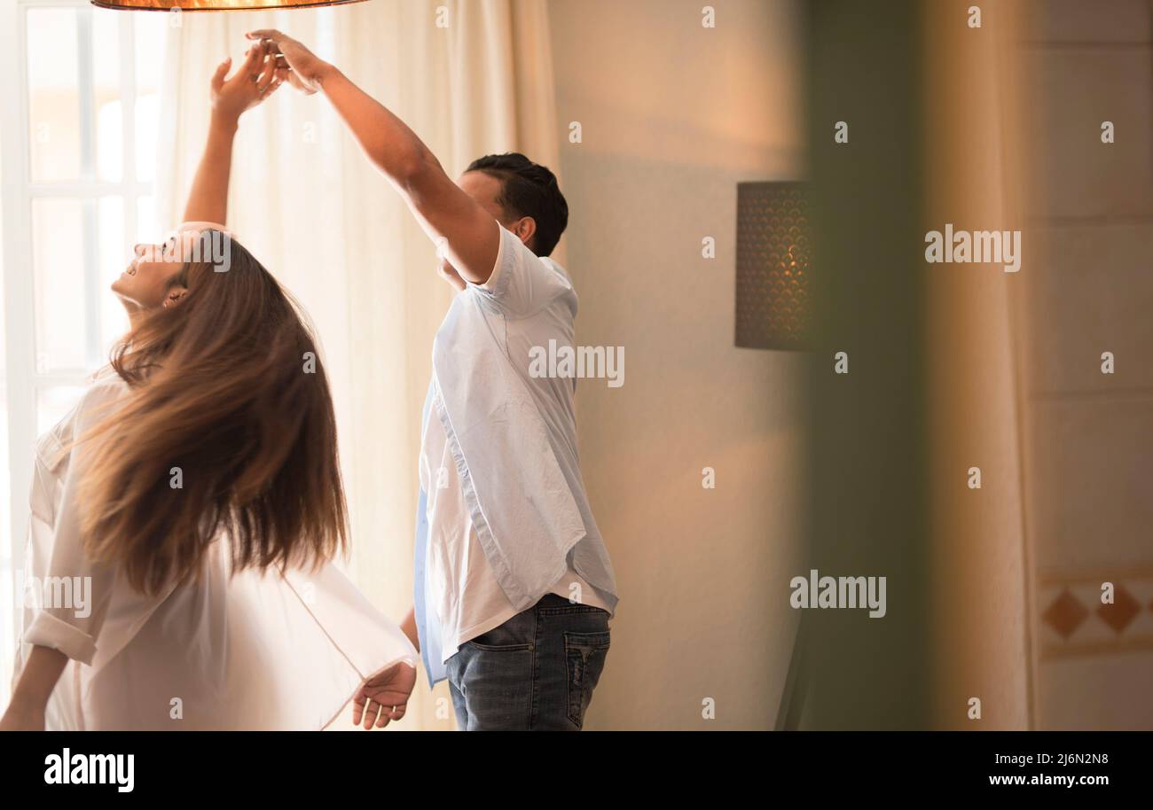 Happy mixed race ethnicity husband and wife feel excited dancing swaying standing at home, smiling overjoyed couple have fun celebrating anniversary Stock Photo