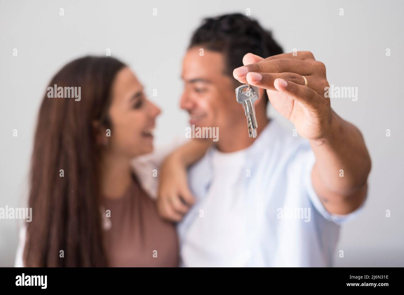 Close up of home keys showed from happy young interracial couple in background - concept of new house purchase and bank loan economy business - real Stock Photo