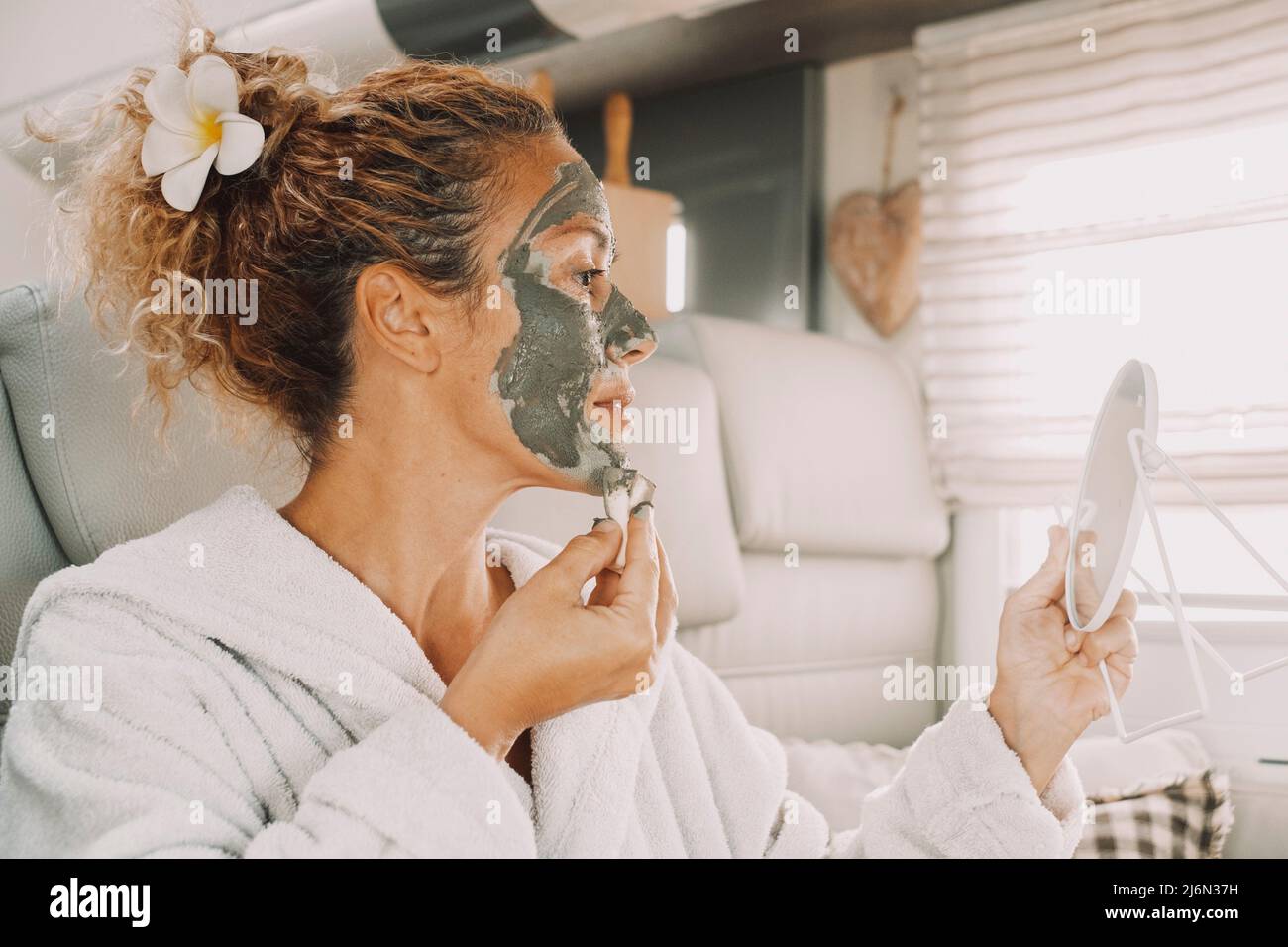 Young adult woman appliying cream beauty skin treatment mask on face using a mirror. Camper van lifestyle and healthy care female people activity. Stock Photo