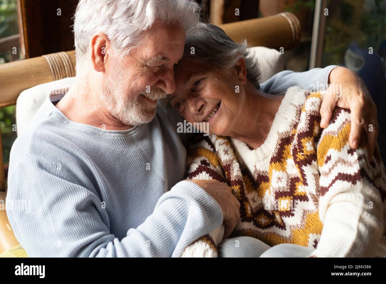 Senior couple in love and tenderness at home sitting together on the sofa. Elderly relationship lifestyle with retired man and woman smiling and Stock Photo