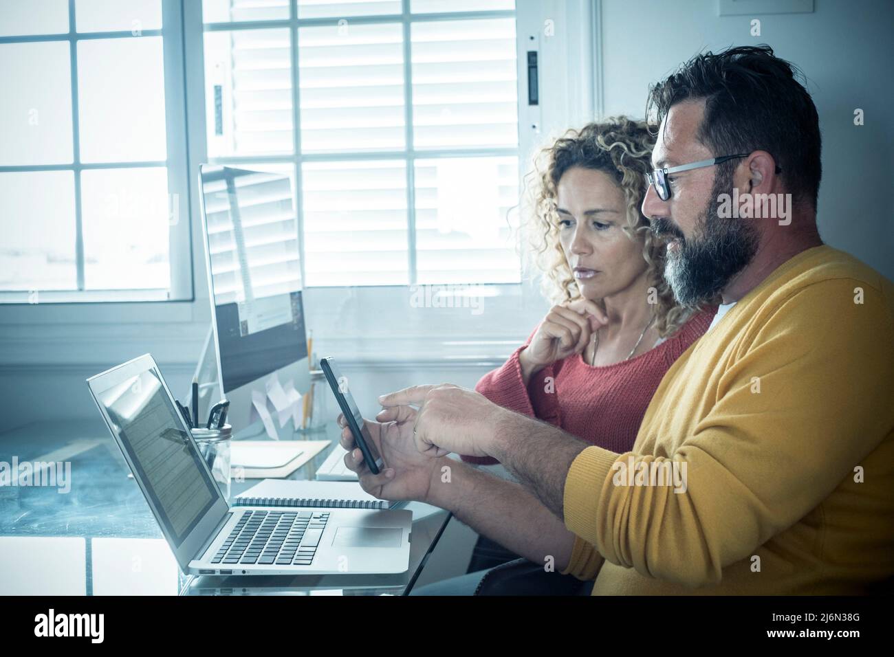 Man and woman team work together in couple at home with technology and online connection laptop computer and phone - smart working and remote workers Stock Photo