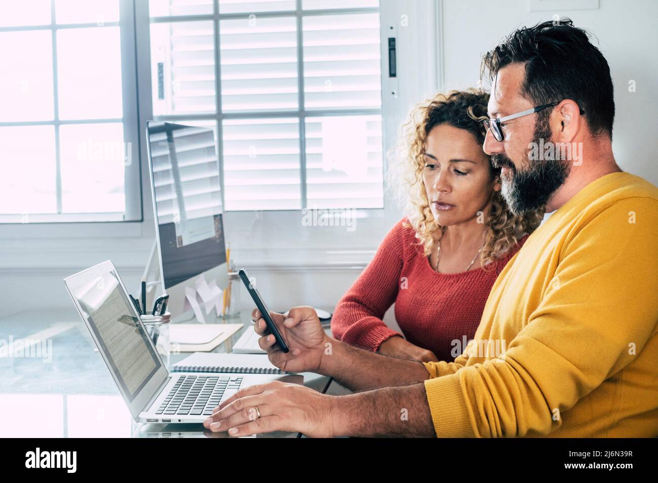 Smart working at home free office lifestyle with adult couple using home and two pc laptop computer on the desktop - modern man and woman online job Stock Photo