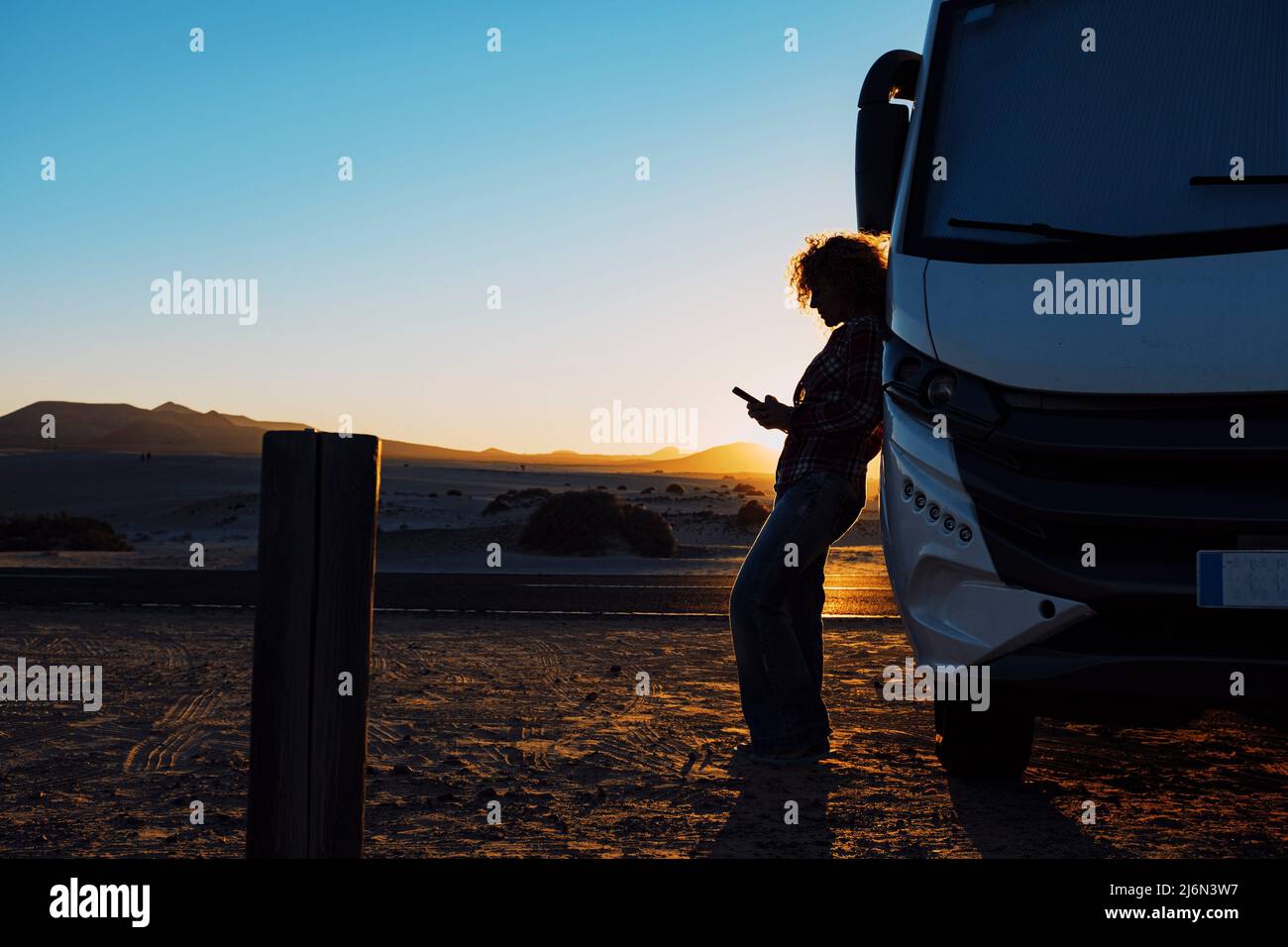 Woman in silhouette against sunset beautiful light. Travel people with camper camping car van for summer vacation or freedom lifestyle. People using Stock Photo