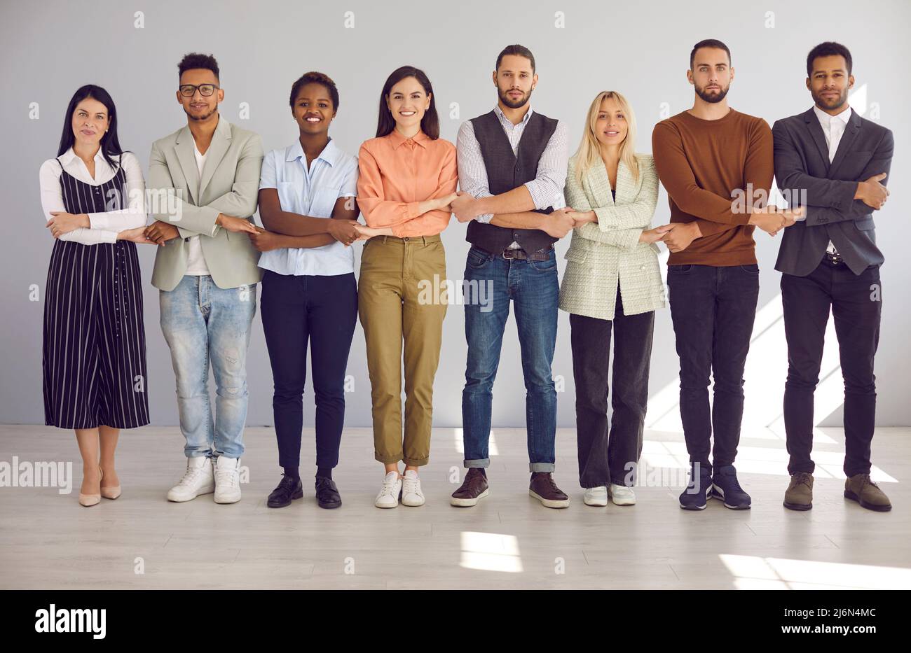 Team of diverse colleagues stand holding hands demonstrating each other