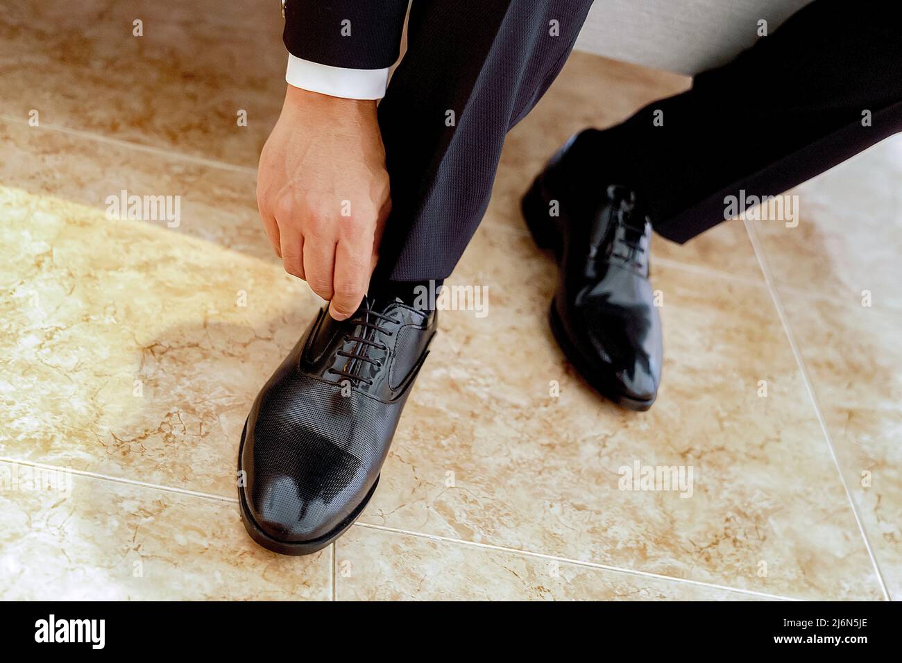 Groom tying the laces of his black shoes on stoneware floor. Stock Photo
