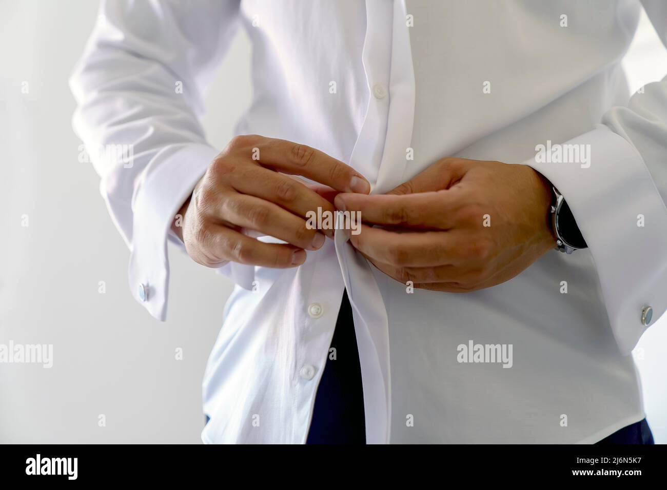 groom getting ready for his wedding buttoning up a white shirt with cuff links. Stock Photo