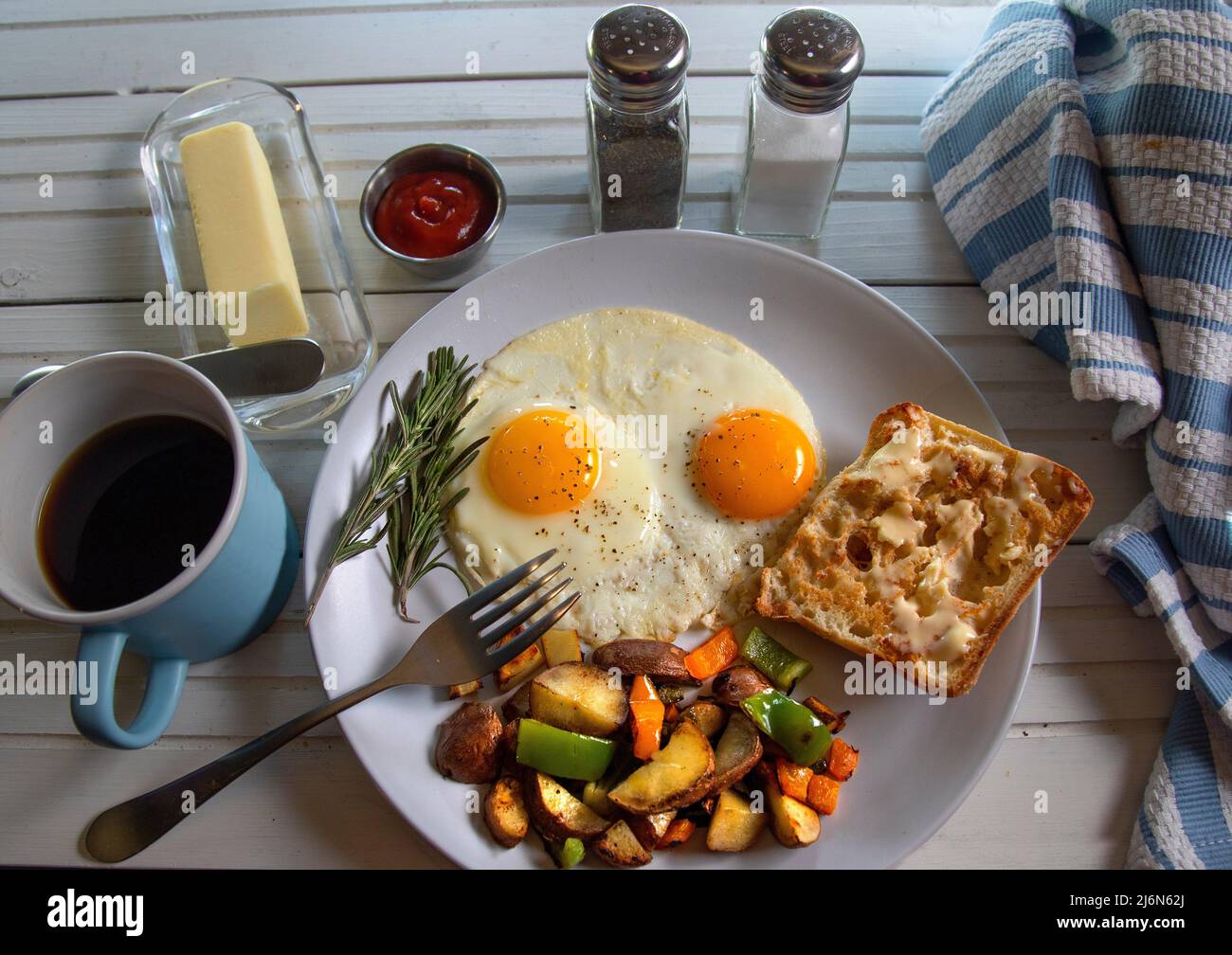 Fried eggs with hash browns and toast and butter on natural white wood table top view. Stock Photo