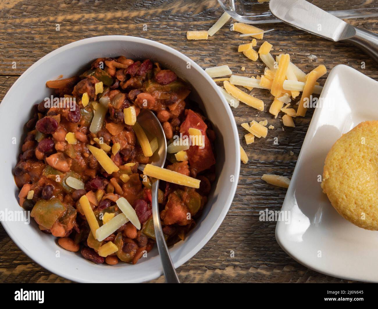 Bowl of vegetarian chilli with cornbread top view on a natural wood table. Stock Photo