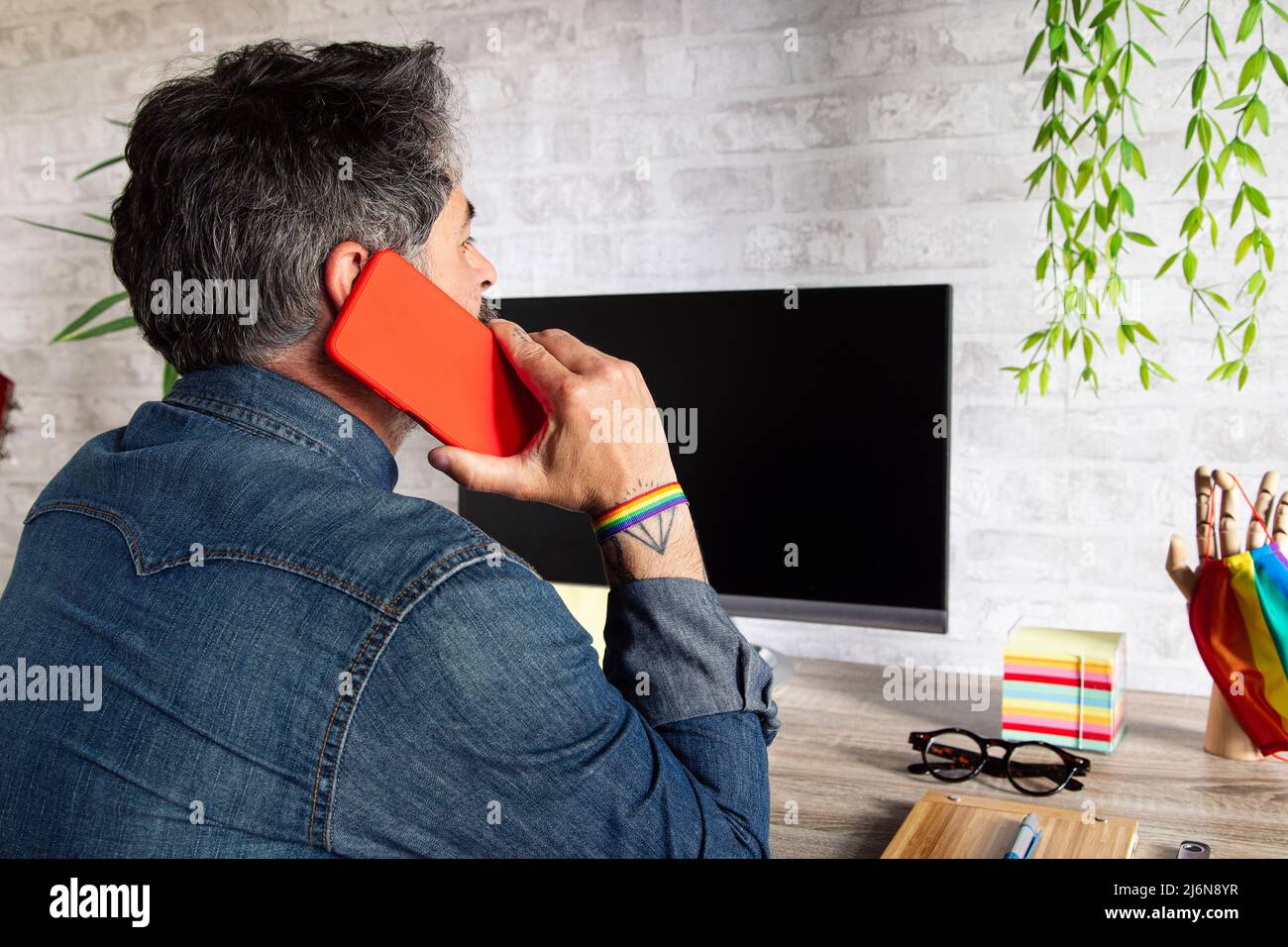 homosexual man talking on the phone in the office with LGBT accessories. Stock Photo