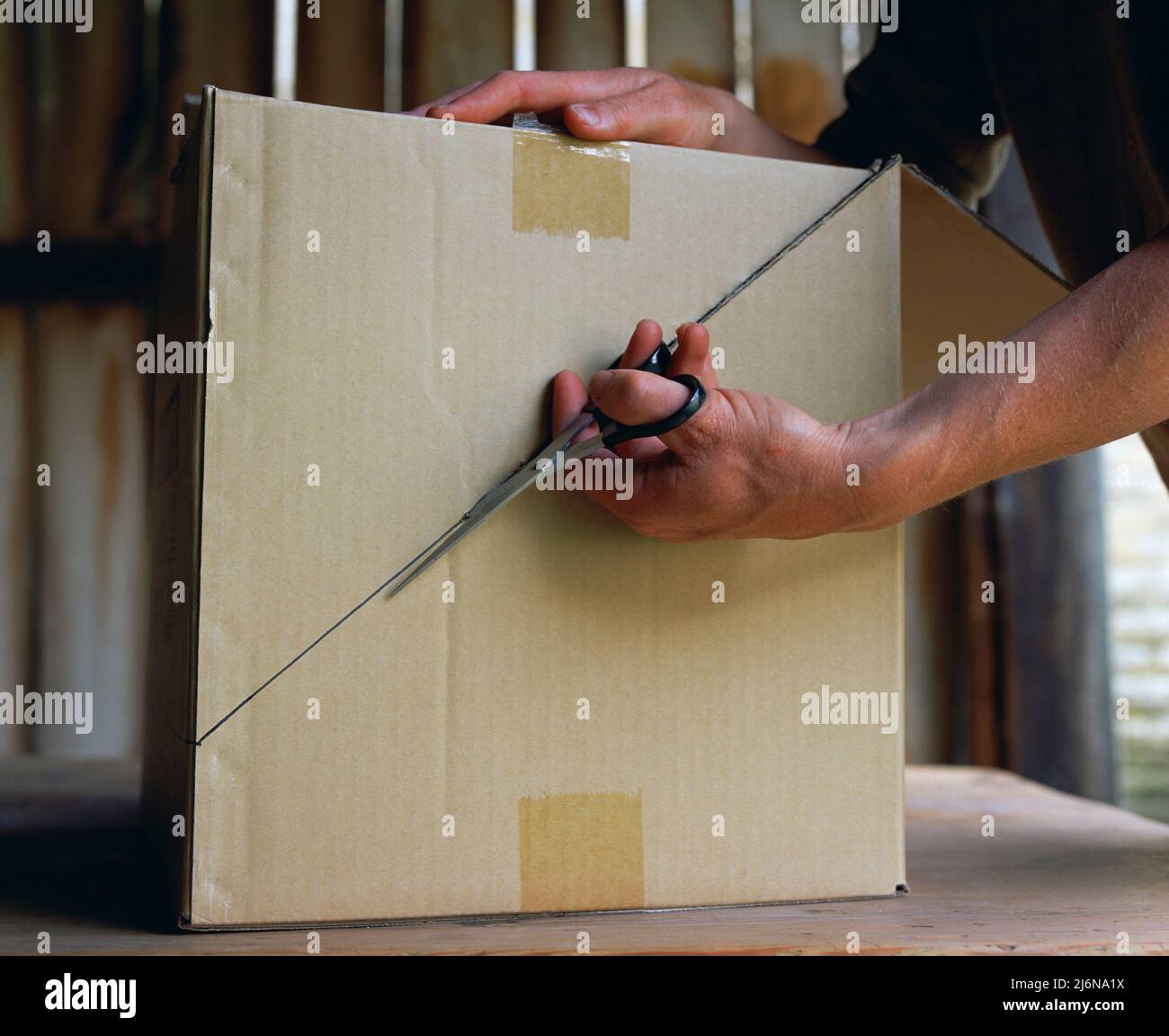 Using a pair of scissors to cut through a diagonal line in the side of a cardboard box. Stock Photo