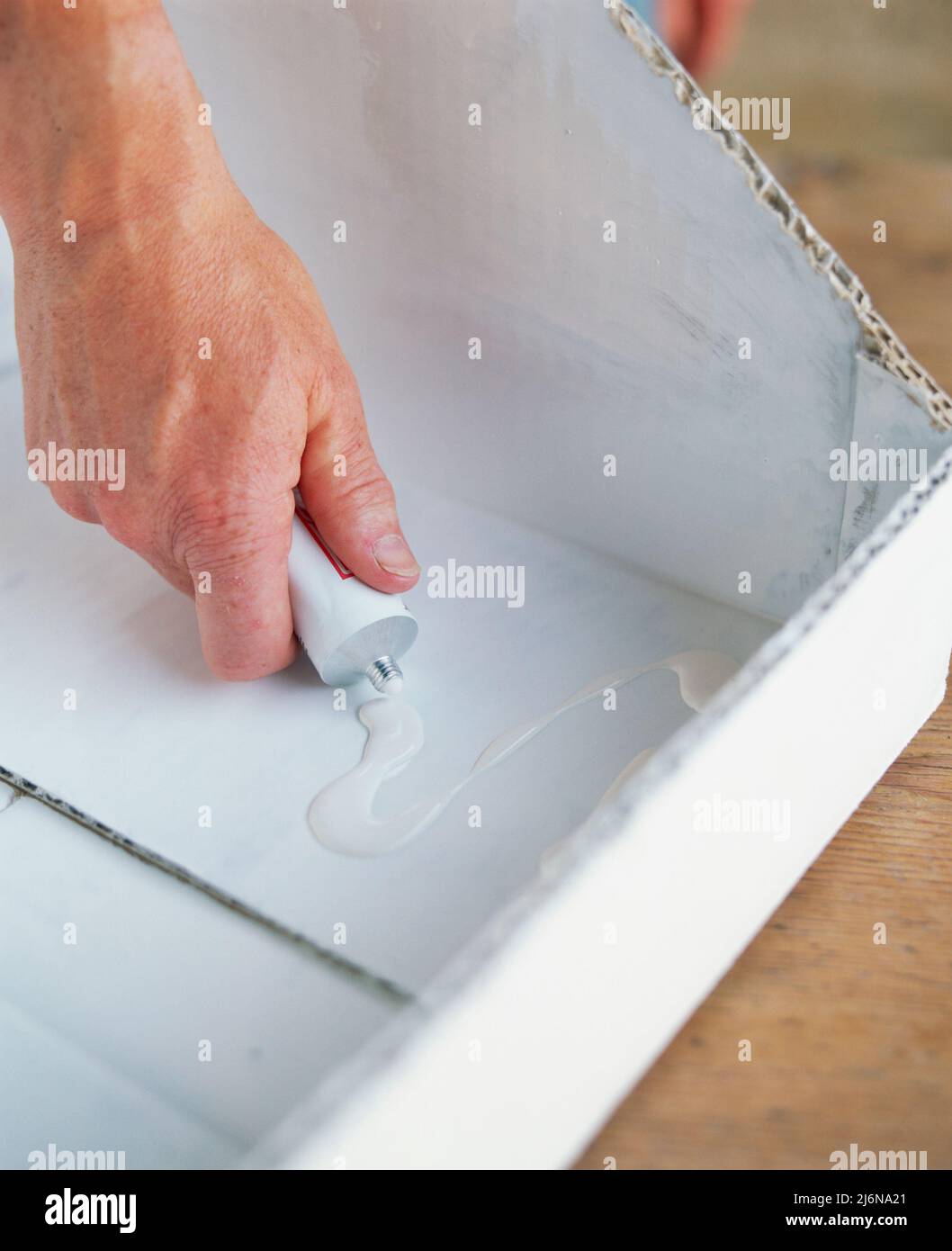 Close-up of squeezing glue from a tube onto the surface of the box that will eventually hold the foil in place. Stock Photo