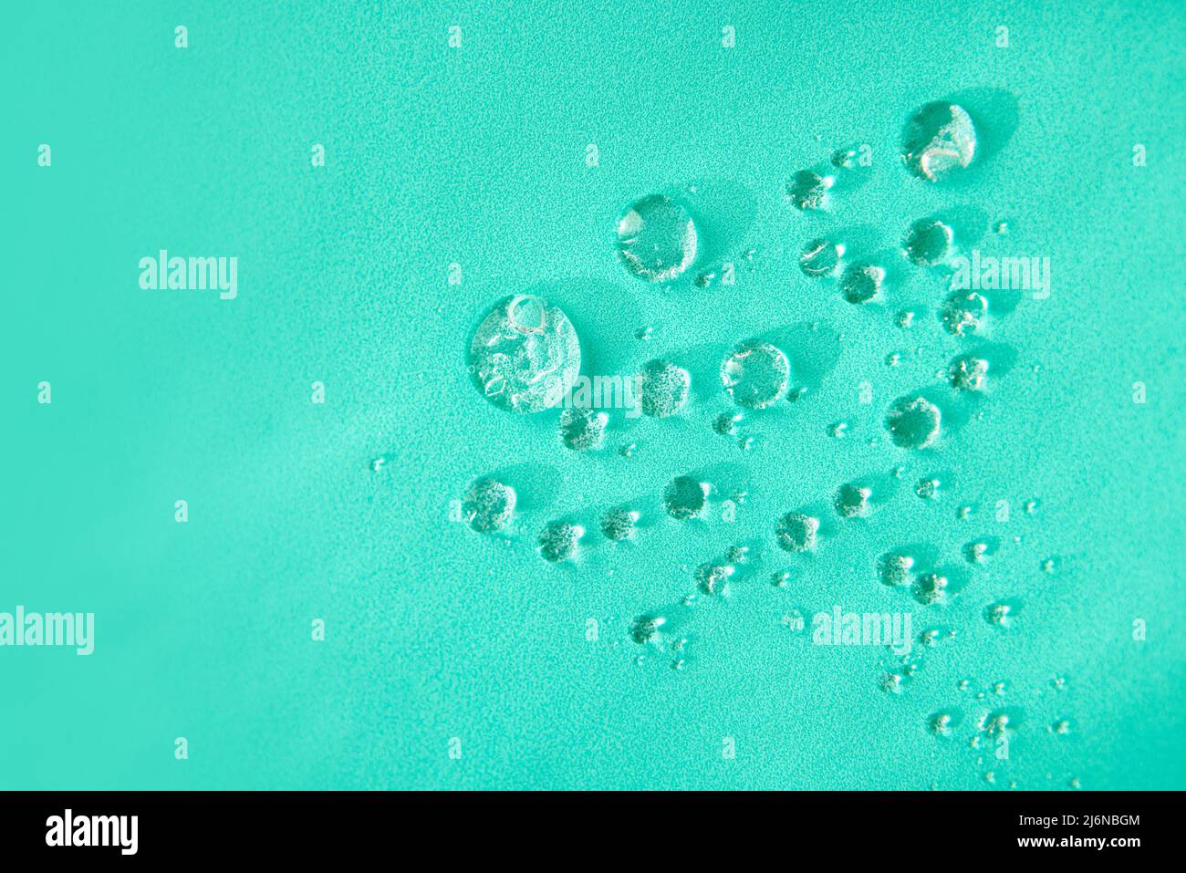 Top view of small transparent round drops of water with different shapes placed on bright green background in light studio Stock Photo