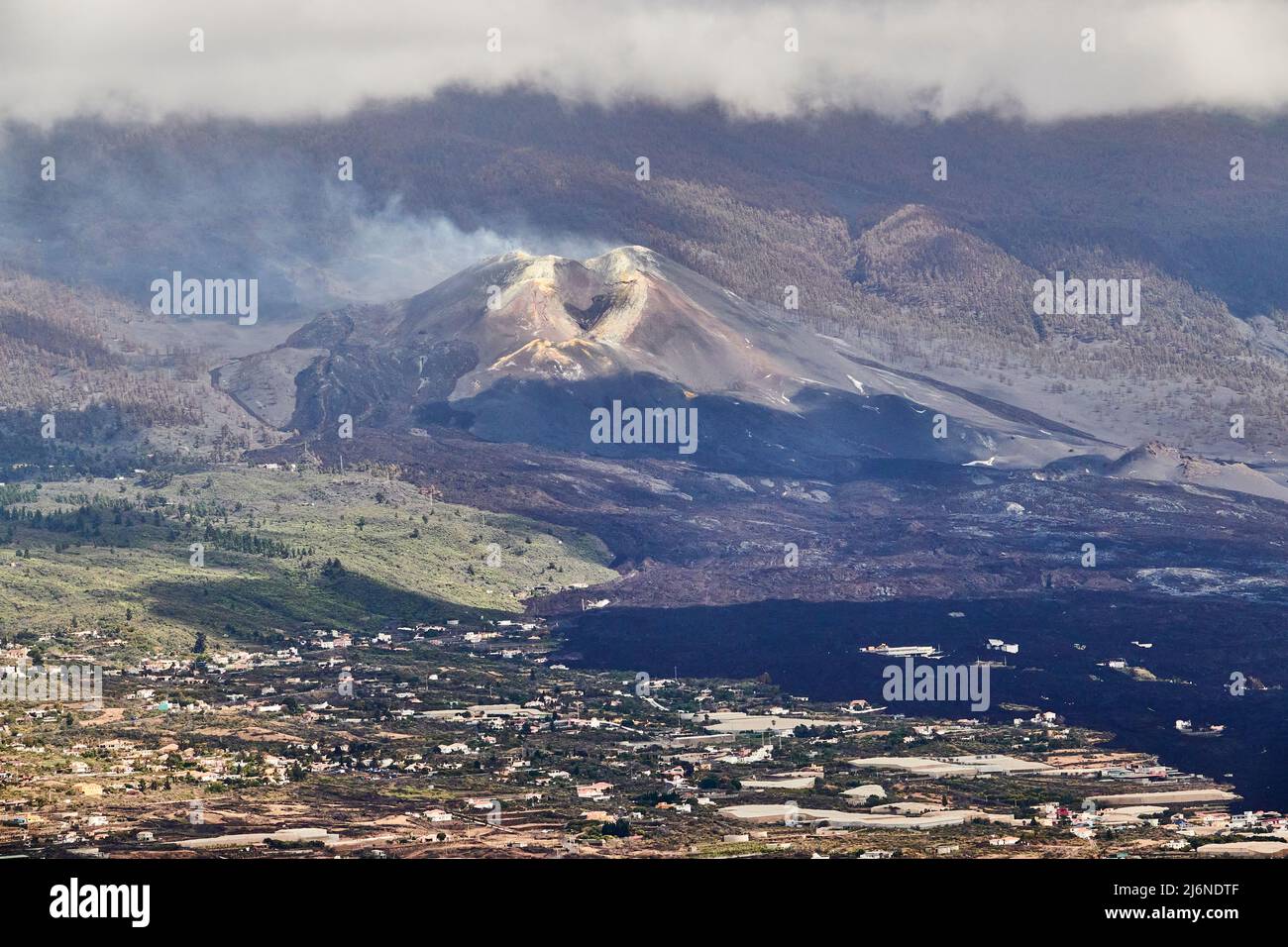 In The Foreground The Village Of El Paso, In The Background A Smoking Still Nameless Volcanic Crater With Sulfur Deposits And Black Magma Flows. El Pa Stock Photo