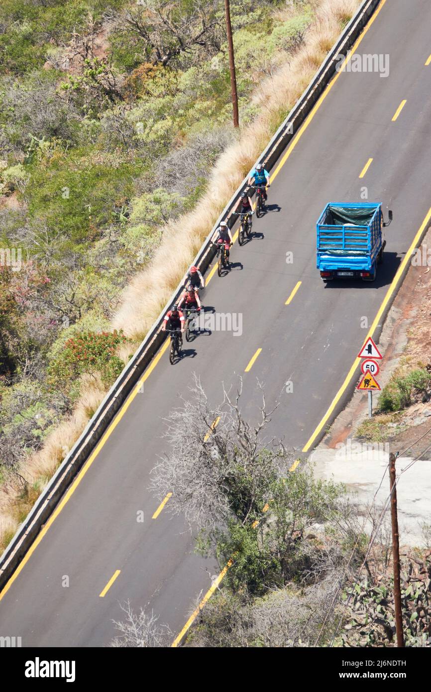 A Group Of Mountain Bikers Crosses A Blue Van On A Asphalt Road With Yellow Street Markings. La Punta, La Palma, Canary Islands, Spain Stock Photo