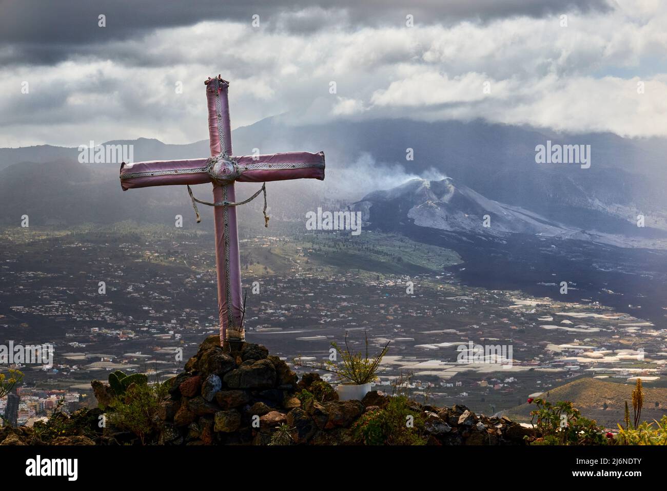 Faith And Natural Disasters - In The Foreground A Decorated Christian Cross, In The Background The Still Nameless Smoking Volcano And Lava Flows. El P Stock Photo