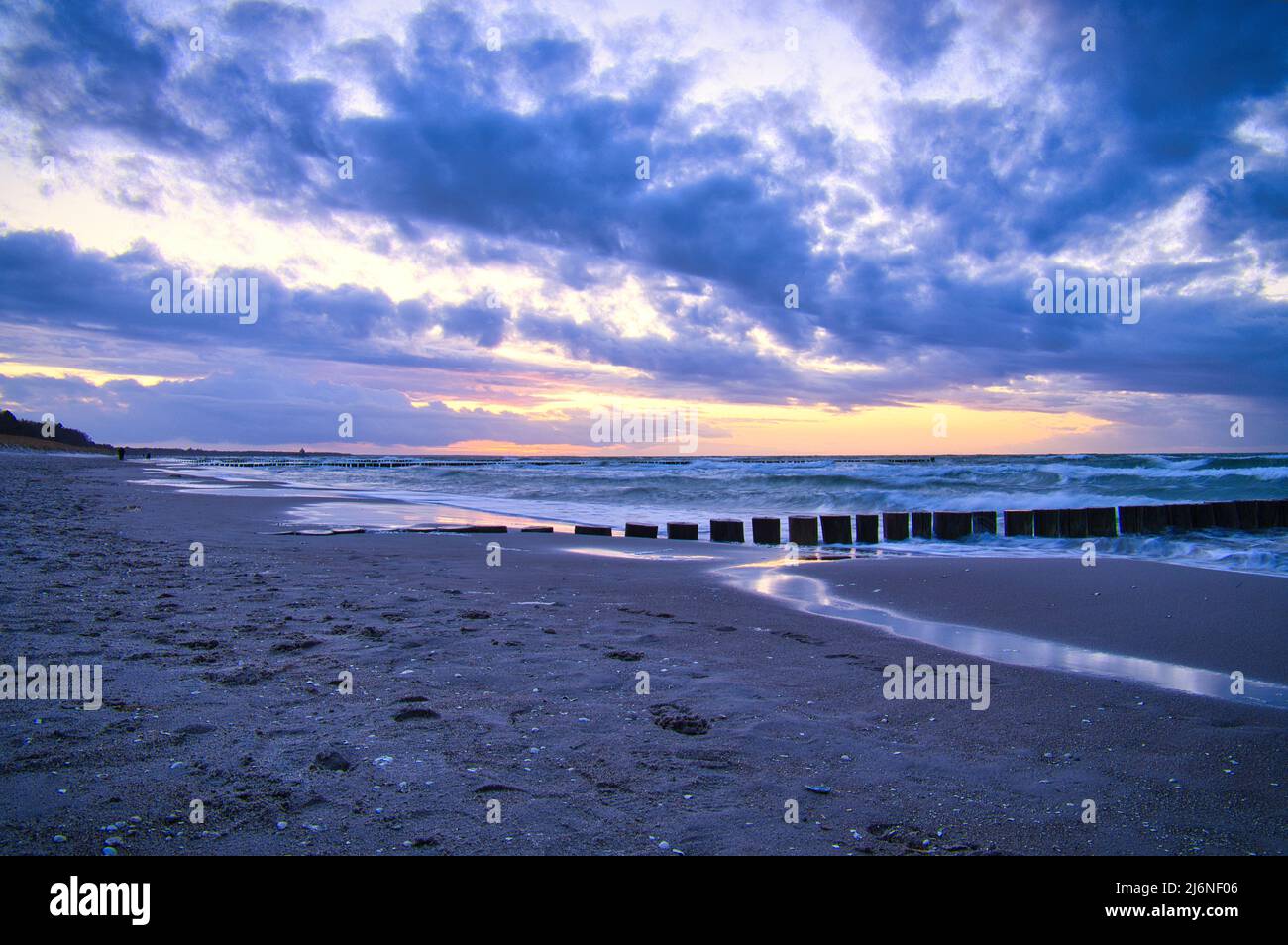 sunset on the beach of the Baltic Sea. Groynes reach into the sea. blue hour with clouds in the sky. Landscape photo in Zingst Stock Photo
