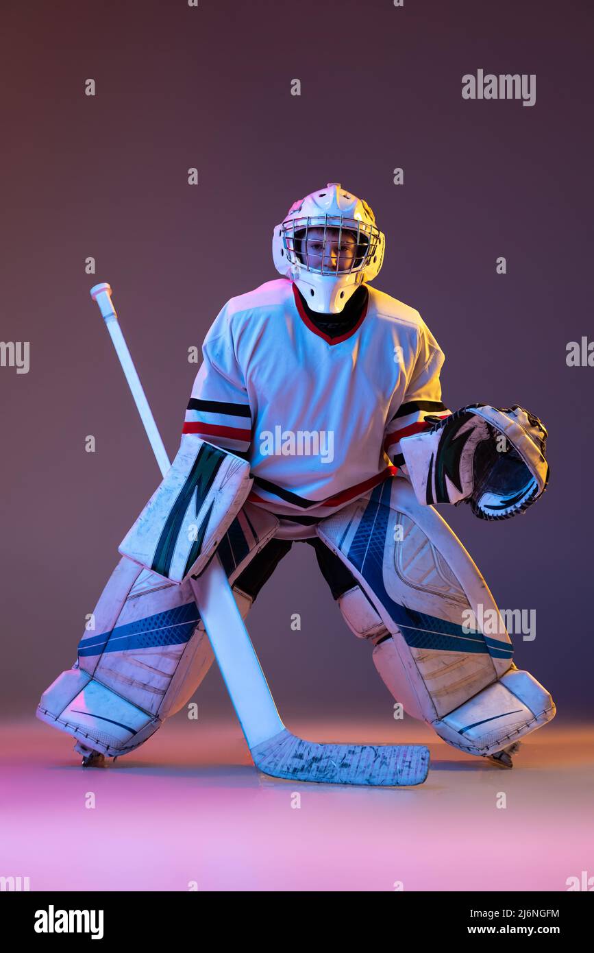 Portrait of concentrated boy, child, goalkeeper, training hockey game isolated over purple background in neon light Stock Photo