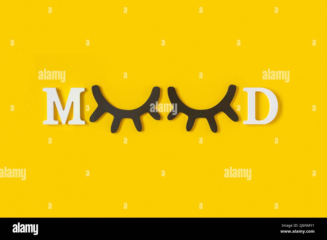 Mood. White letters and wood black eyeleshes on yellow background. Creative moning concept. Top view, Flat lay. Greeting card. Stock Photo