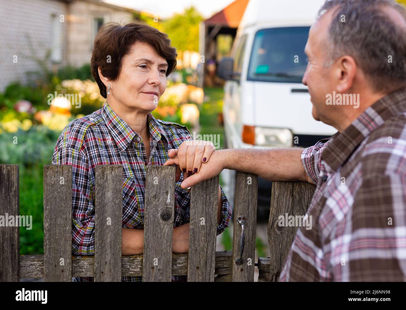 neighbors man and woman chatting near the fence in the village Stock Photo