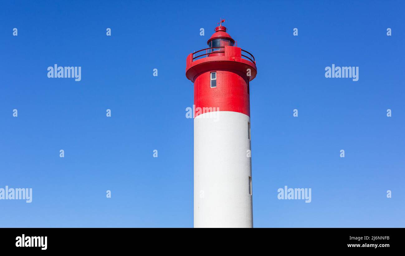Red white lighthouse beacon close-up structure for warning safety for ship boat vessels of ocean bad weather storms  against blue sky on coastline. Stock Photo