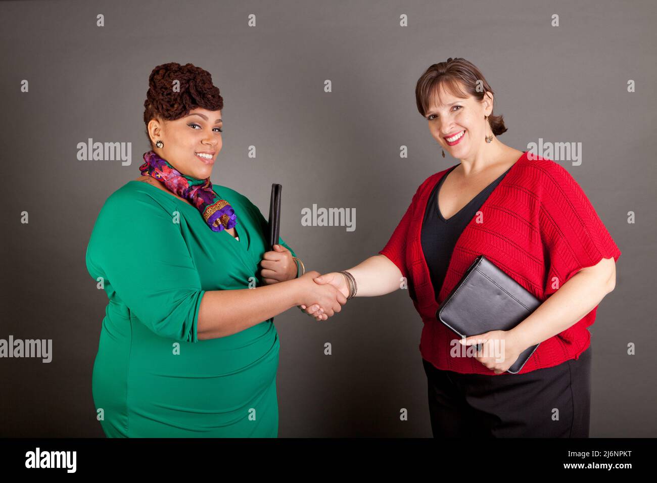 Happy, smiling plus size women of different races shaking hands holding business portfolios Stock Photo