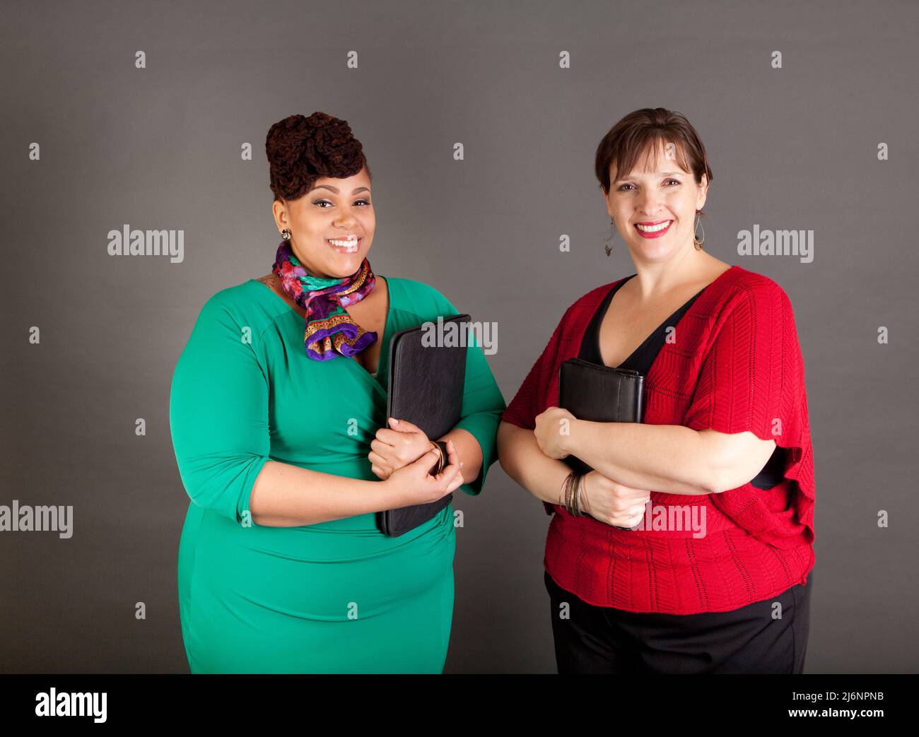 Happy, smiling plus size women of different races looking at the camera wearing bold colors holding traditional business portfolios Stock Photo