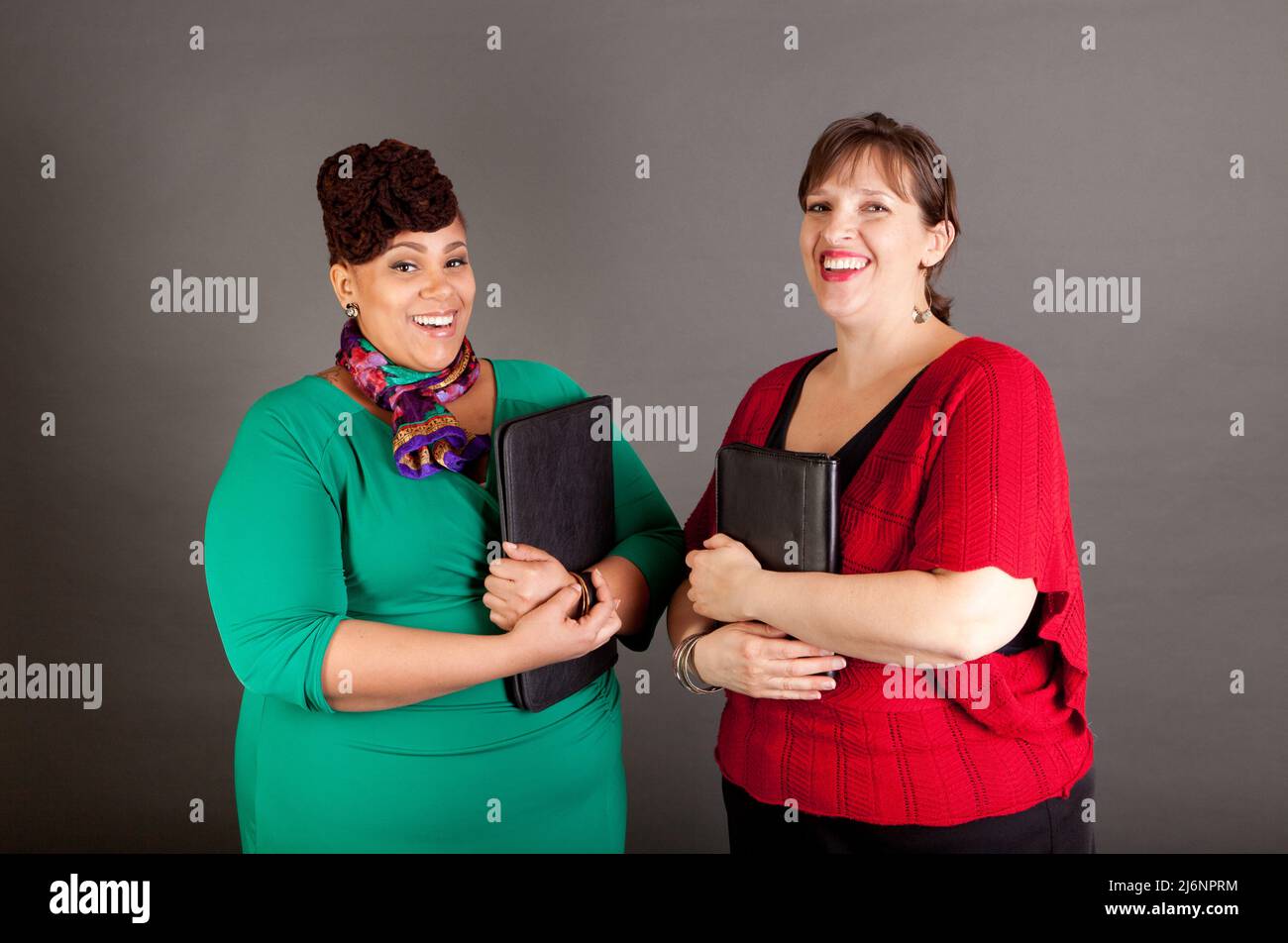 Happy, smiling plus size women of different races looking at the camera wearing bold colors holding traditional business portfolios Stock Photo