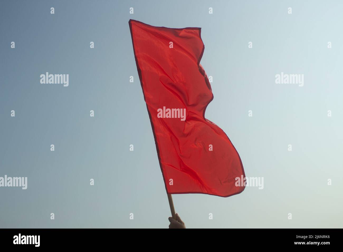 Red flag in his hand against sky. Red matter on pole. Signal to start start. Flag developing in wind. Stock Photo