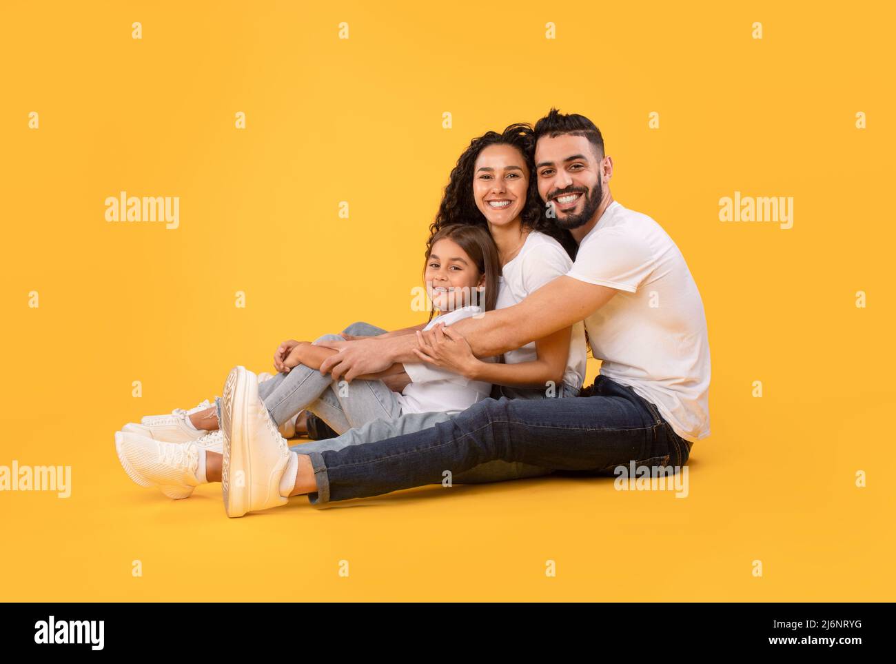 Arabic Family Of Three Embracing Together Sitting Over Yellow Background Stock Photo