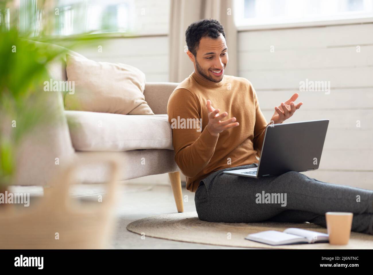 Arab guy making videocall using laptop sitting on floor Stock Photo