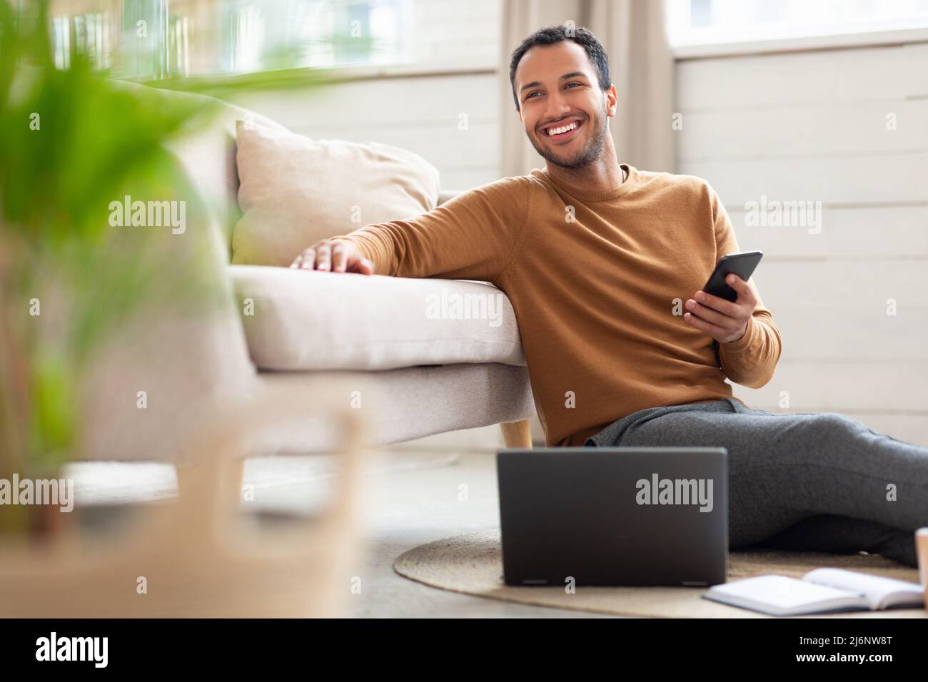 Young Arab man holding phone using pc at home Stock Photo