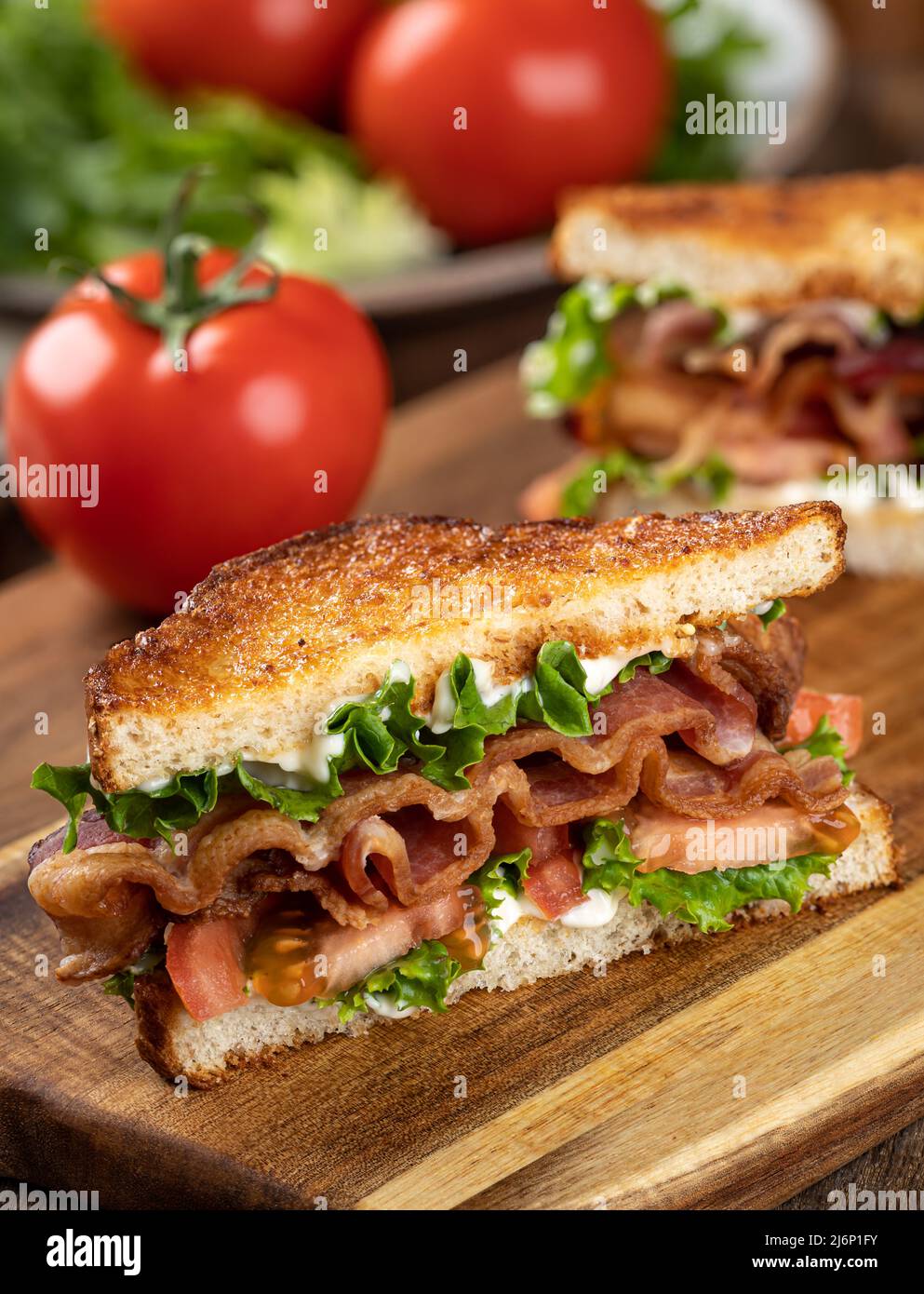 Blt sandwich made with bacon, lettuce and tomato on toasted whole grain bread cut in half on a wooden cutting board Stock Photo