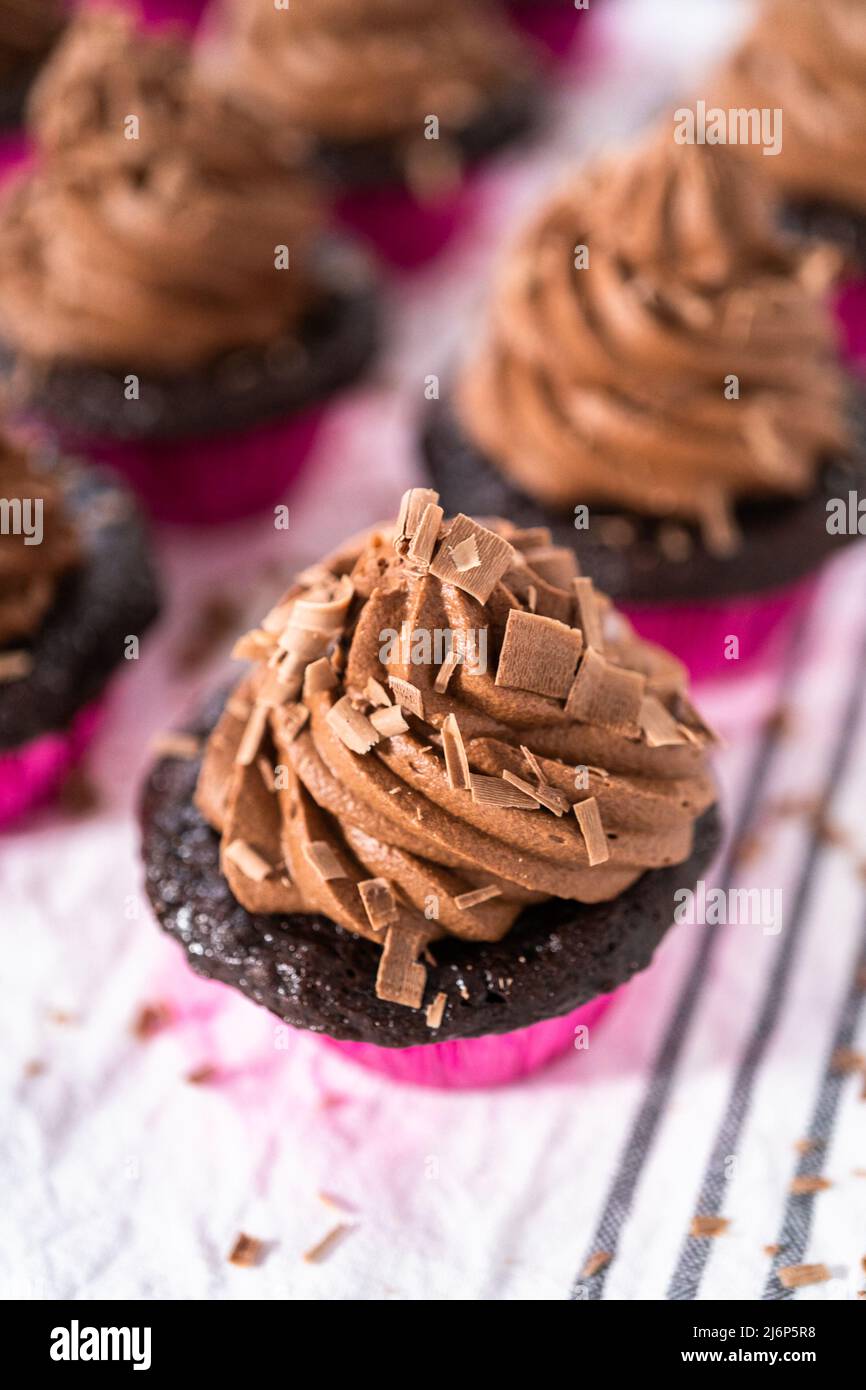 Piping chocolate ganache frosting on top of chocolate cupcakes Stock
