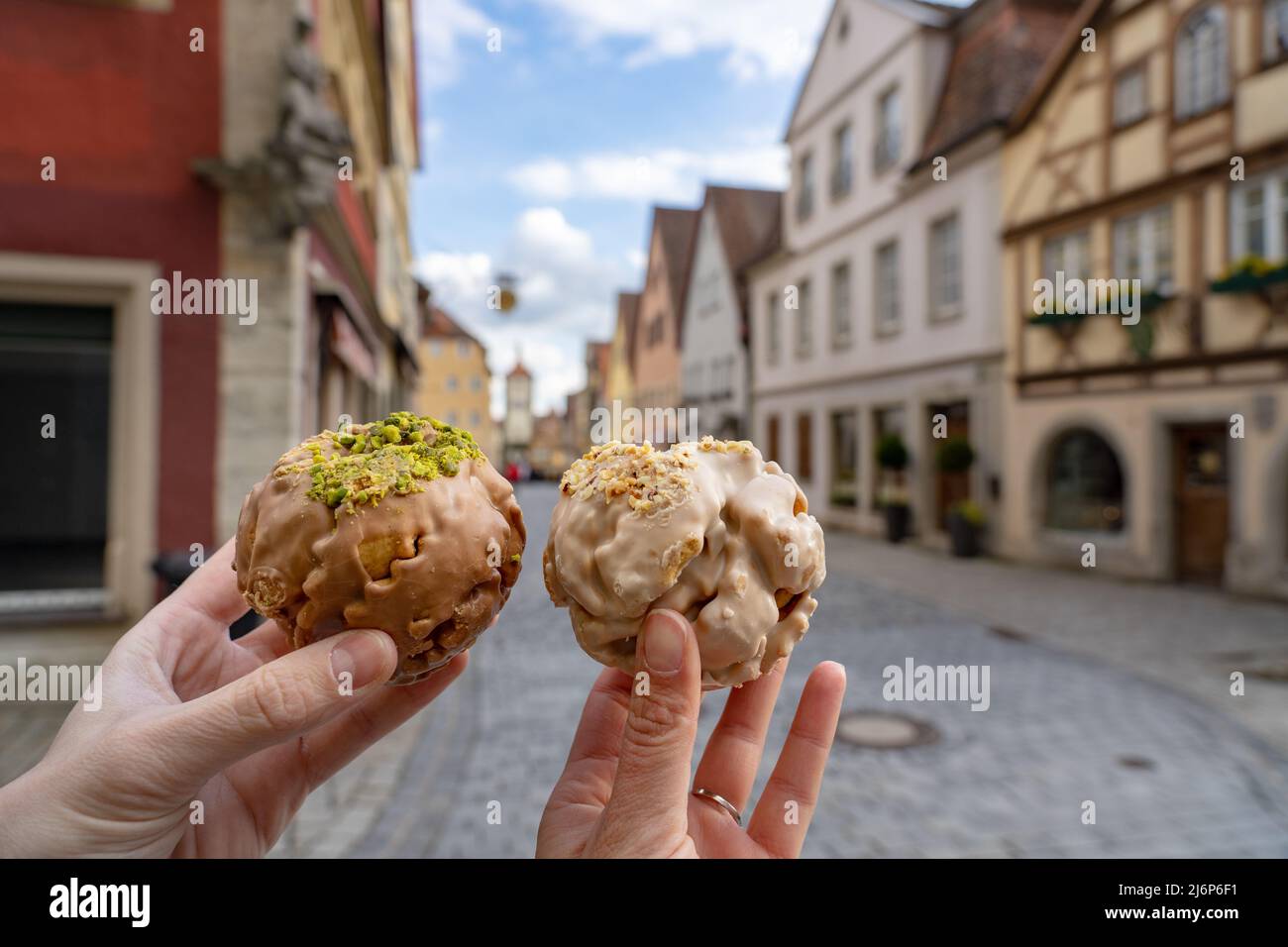 eating traditional schneeball snowball cake together the cake of the romantic Rothenburg ob der Tauber with timbered Fachwerkhaus syle houses in Bavar Stock Photo