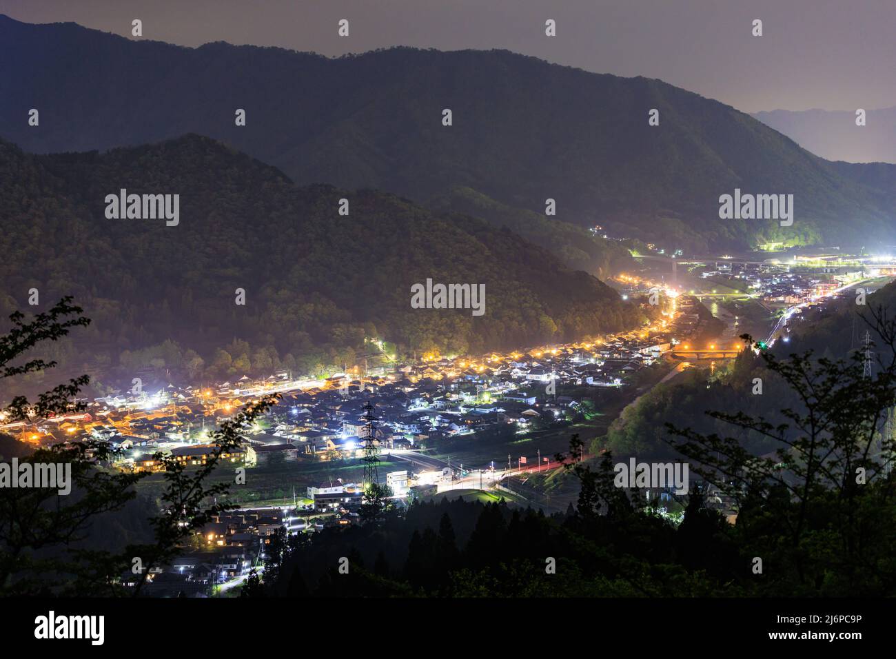Small village lit up between dark mountains at night Stock Photo