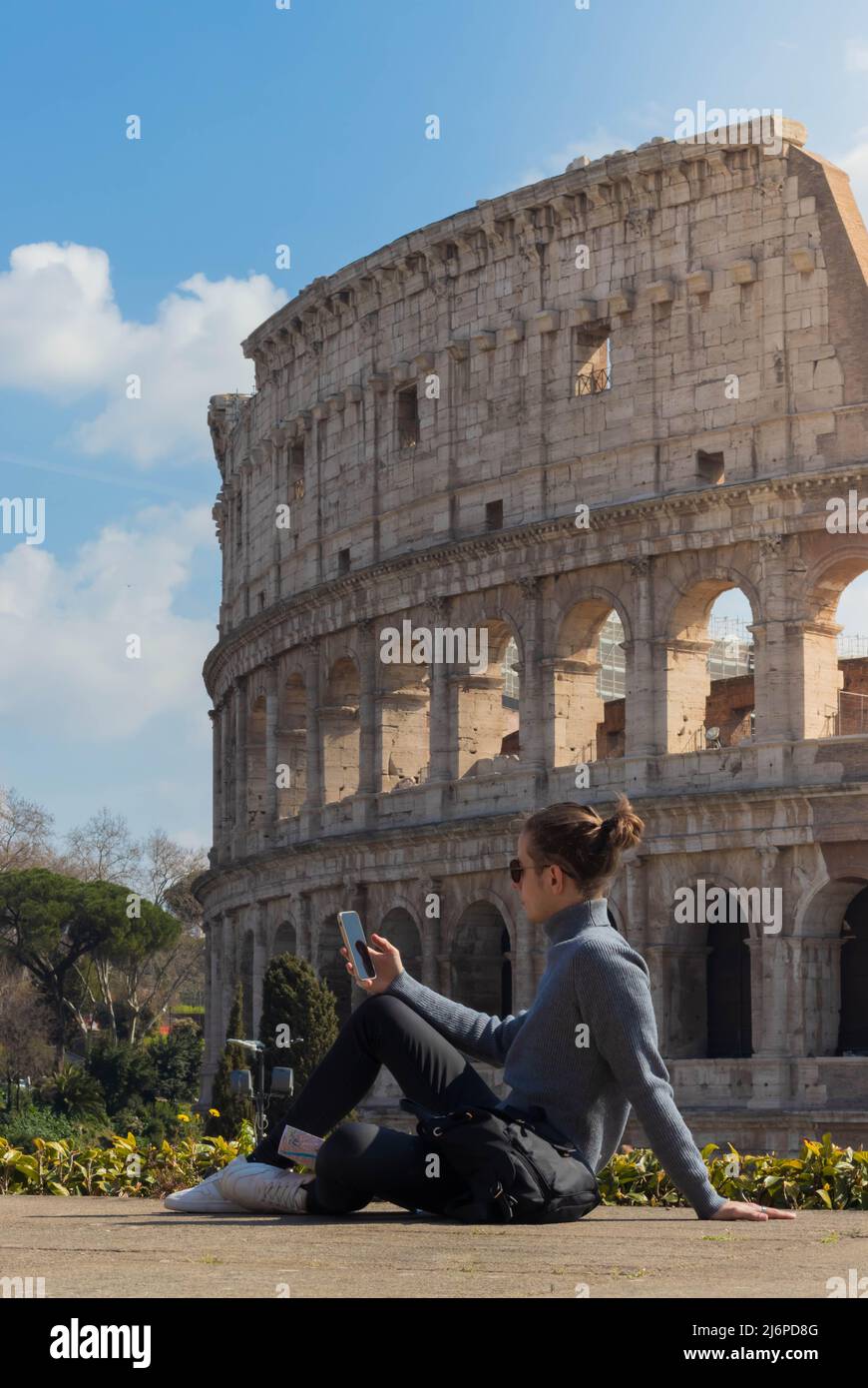 Young man with bun on his smartphone while sitting relaxed resting with the Rome coliseum in the background Stock Photo