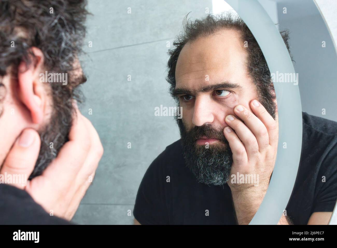 Middle-aged man looking tired and depressed in the bathroom mirror Stock Photo