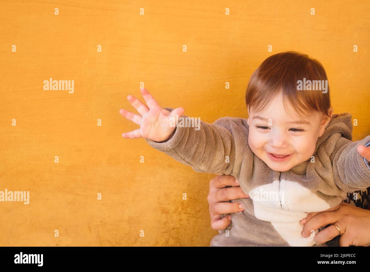 Adorable baby toddler boy wearing a warm winter onesie jumpsuit against a bright orange wall background Stock Photo
