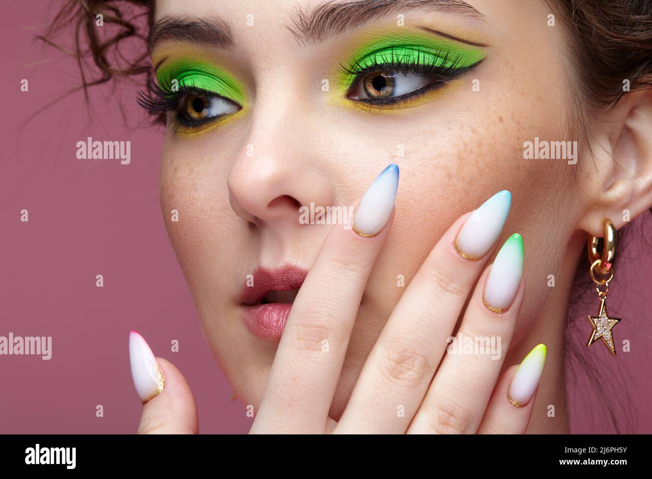 Portrait of young woman with hand near face. Female with unusual green eyes shadows makeup. Girl with nails with multi-colored manicure. Stock Photo